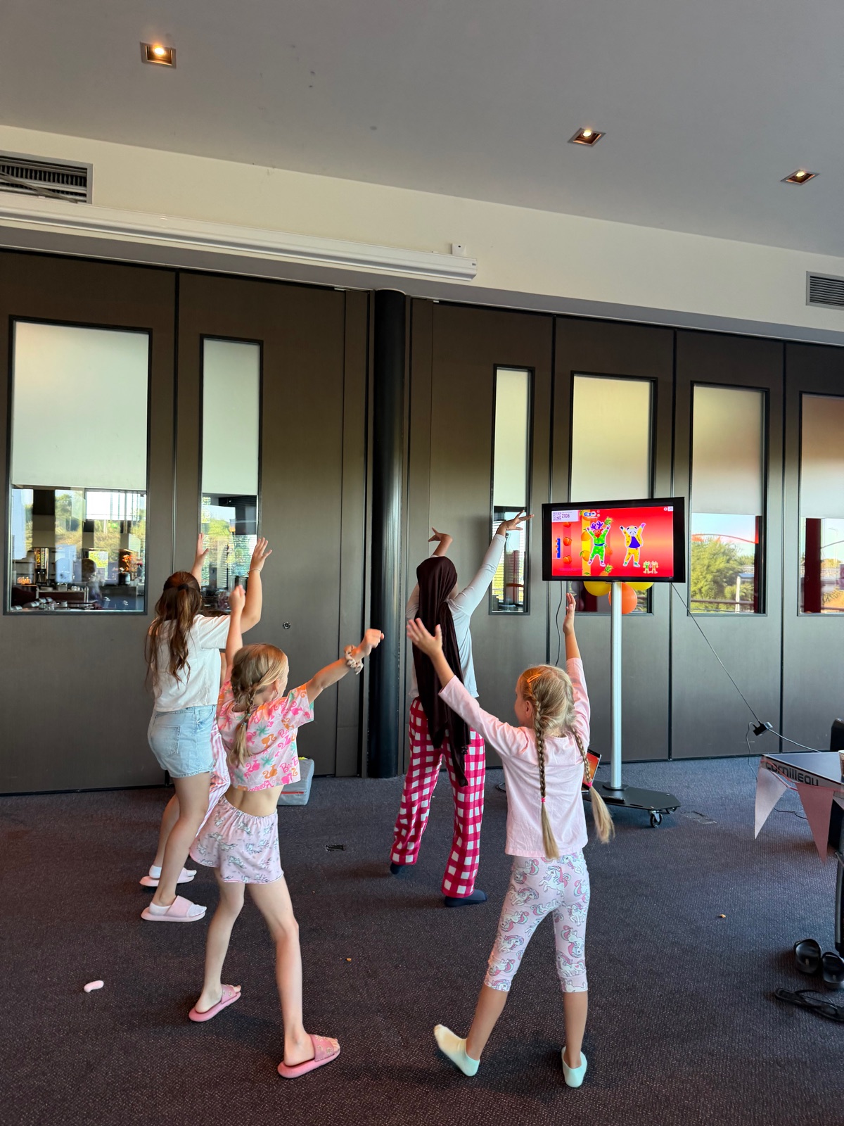 Meiden in pyjama dansen Just Dance voor de televisie, van achteren gezien